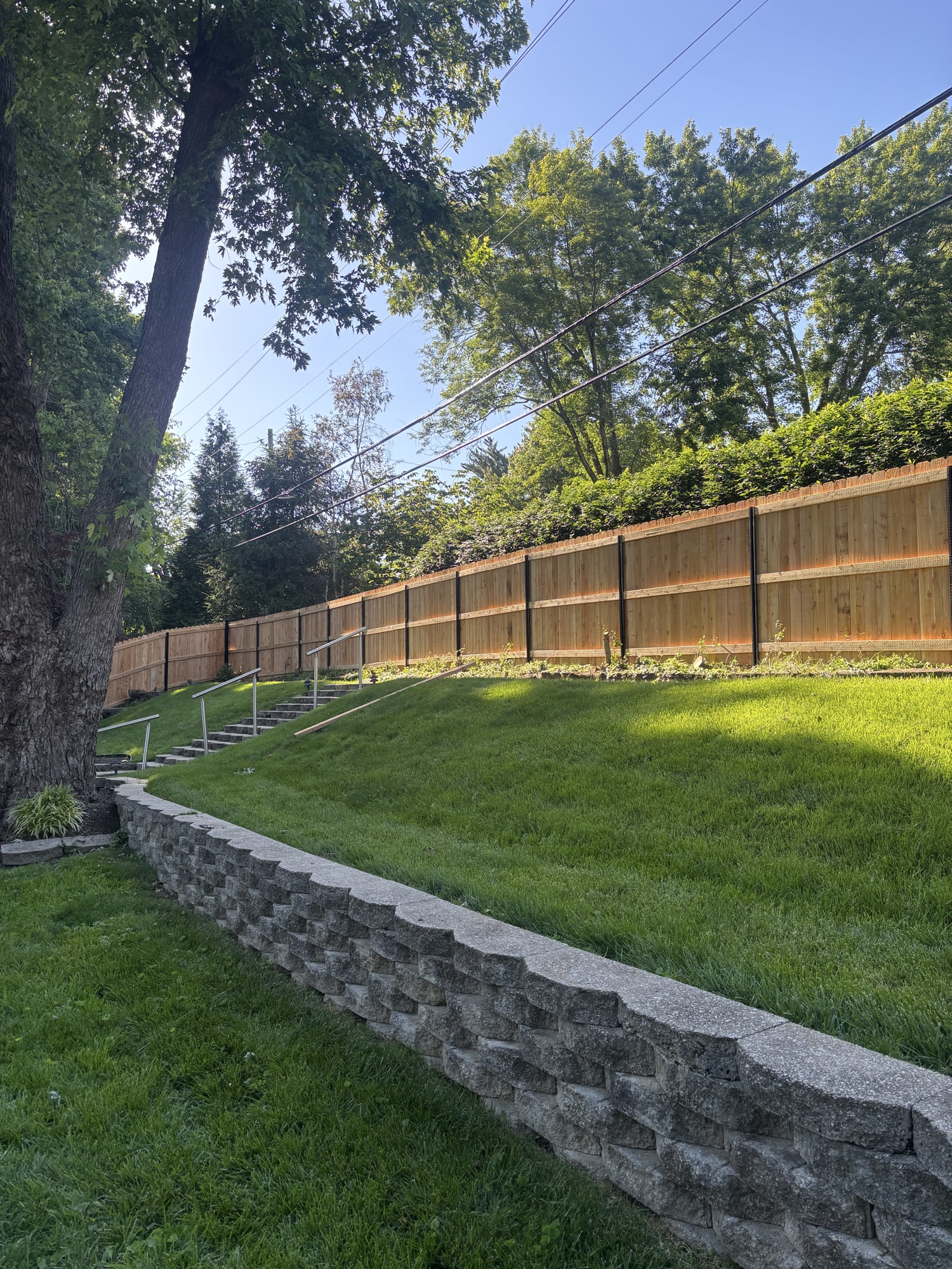 Stone retaining wall running along hillside with cedar fence
